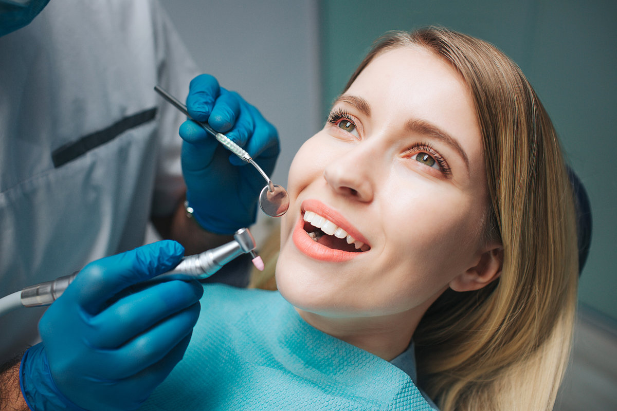 Close up of nice young woman sitting in dentistry chair in room. She keep mouth opened and look up. Dentist hold medical equipment for teeth treatment