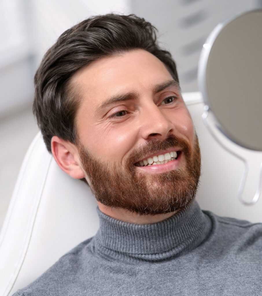 Man looking at his new dental implants in mirror indoors