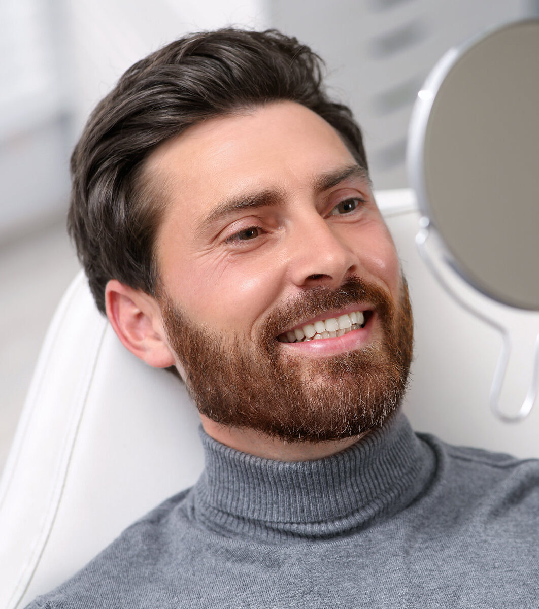 Man looking at his new dental implants in mirror indoors