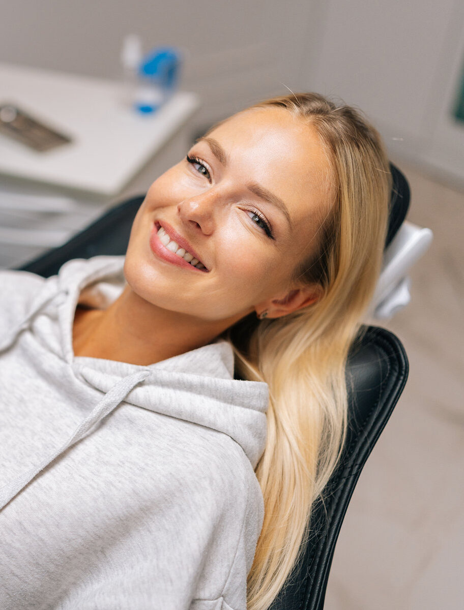 Portrait of charming young woman patient with perfect white teeth and smile satisfied after dental treatment lying on dental chair in dentistry clinic. Female dentist in gloves examining teeth.